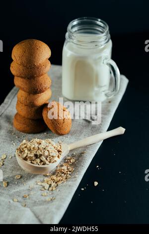 Stapel von frischen Haferflocken mit Milch im Glas, rohe Haferflocken in großen Holzlöffel auf schwarzem Hintergrund. Stillleben Stockfoto