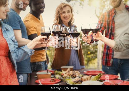 Fröhliche Familie trinkt Rotwein und jubelt draußen - Beste Freunde toasten zusammen während der Weinprobe Party auf dem Land - Multigenera Stockfoto