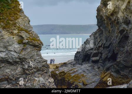 Ein weiter Blick durch eine Lücke in den Klippen von Surfern im Meer am Great Western Beach in Newquay in Cornwall in Großbritannien. Stockfoto