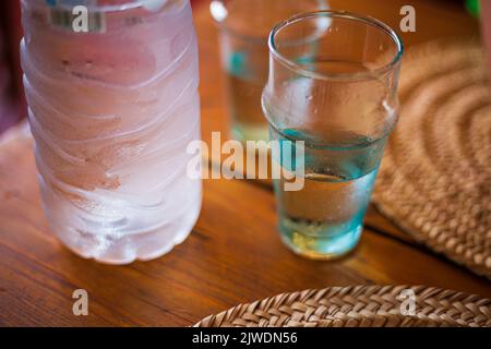 Kaltes, frisches Plastikwasser und Trinkglas mit feuchten, nassen Tropfen auf einem braunen Holztisch aus nächster Nähe Stockfoto