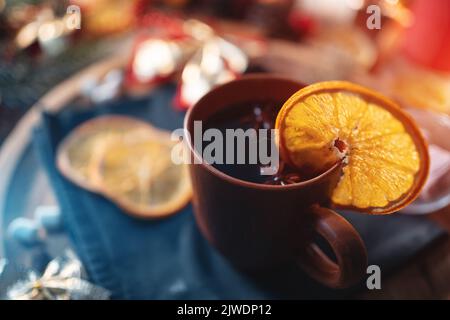 Glühwein aus Rotwein in Tasse mit Orange, weihnachtlicher Dekorationstisch mit Kerzen Stockfoto