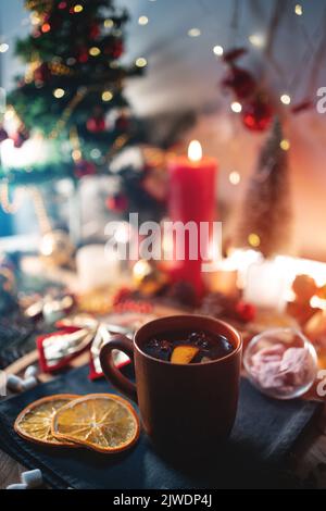 Glühwein aus Rotwein in Tasse mit Orange, weihnachtlicher Dekorationstisch mit Kerzen Stockfoto