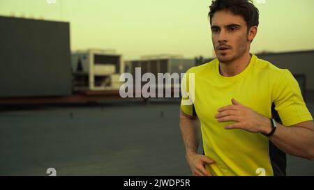 Junge Brünette Sportler läuft auf dem Dach des Gebäudes am Abend, Stock Bild Stockfoto