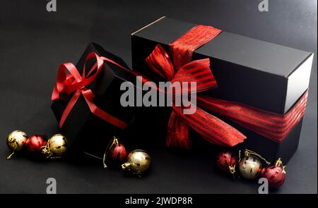 Komposition von Geschenken in verschiedenen Formen, eingewickelt in schwarzes Geschenkpapier mit einem roten Band und einer Schleife auf schwarzem Hintergrund. Seitenansicht. Speicherplatz kopieren. Stockfoto