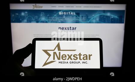 Person, die ein Smartphone mit dem Logo des US-amerikanischen Fernsehunternehmens Nexstar Media Group Inc. Auf dem Bildschirm vor der Website hält. Konzentrieren Sie sich auf die Telefonanzeige. Stockfoto