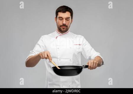Männlicher Koch in der Jacke kocht Essen auf der Bratpfanne Stockfoto