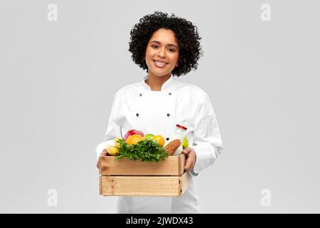 Glückliche lächelnde Köchin mit Essen in Holzkiste Stockfoto