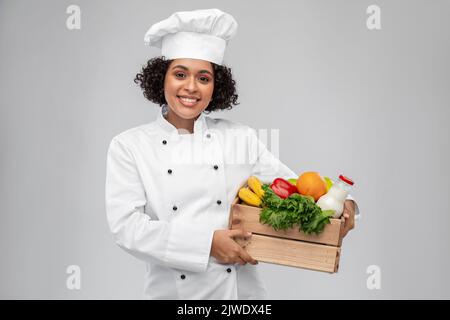 Glückliche lächelnde Köchin mit Essen in Holzkiste Stockfoto