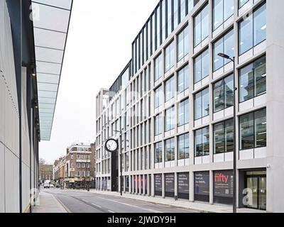 Blick auf die Straße entlang der verglasten Gebäudefassade mit großer Außenuhr. 50 Eastbourne Terrace, London, Großbritannien. Architekt: Sheppard Robson, 2021. Stockfoto