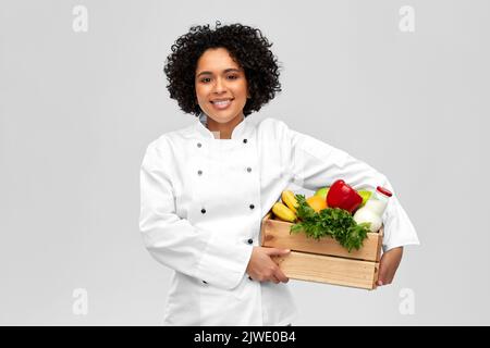 Glückliche lächelnde Köchin mit Essen in Holzkiste Stockfoto