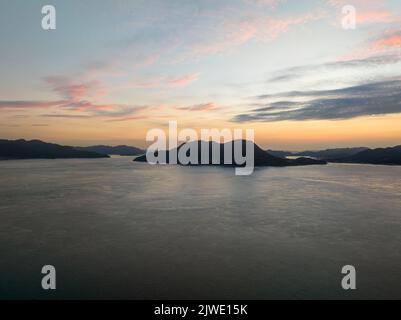 Luftaufnahme der kleinen Küsteninsel, die vor dem Himmel vor Sonnenaufgang geschildet wurde Stockfoto