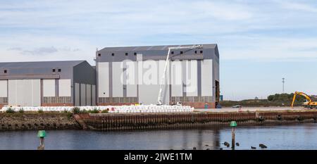 Zwei Männer auf der Oberseite einer Kirschpflückmaschine, die Arbeiten auf dem Dach eines großen Industriegebäudes in Middlehaven, Middlesbrough, England, Großbritannien, durchführen Stockfoto