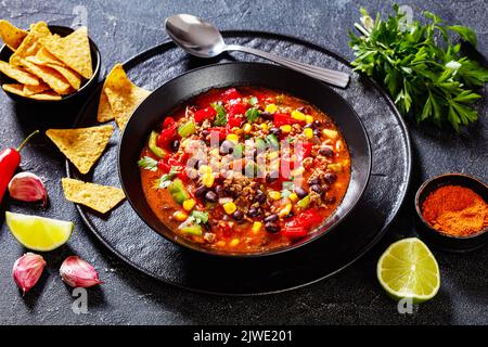 taco-Suppe aus Hackfleisch, Tomaten, gehackten grünen Chilis, Zwiebeln, Mais, Rote Bohnen und Taco-Würze in schwarzer Schale, Landschaftsansicht Stockfoto