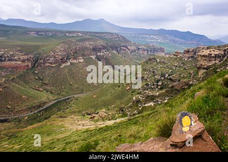 Die dramatischen hohen Gipfel des Drakensbergs, mit einem einzigen gelben Wanderzeichen im Vordergrund Stockfoto