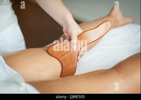 Eine Therapeutin führt eine Maderotherapie an den Beinen einer Frau mit einem Massagespatel aus Holz durch Stockfoto