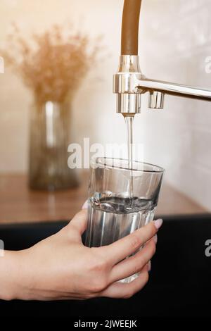 Frau, die in der Küche Trinkglas mit Leitungswasser füllte. Konzept für sauberes Trinkwasser zu Hause. Frisches Getränk gießen. Wasserqualitätsprüfung Konz Stockfoto