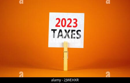 2023 Steuern Neujahr Symbol. Weißes Papier mit Worten 2023 Steuern, Clip auf Holzlasche. Schöne orange Tisch orange Hintergrund. Business und 2023 Stockfoto