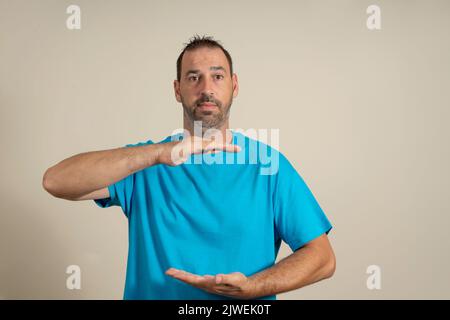 Glücklicher hispanischer Mann, der etwas zwischen seinen Händen zeigt, Produktmarketing-Werbekonzept mit Kopierfläche auf beigem Hintergrund. Stockfoto