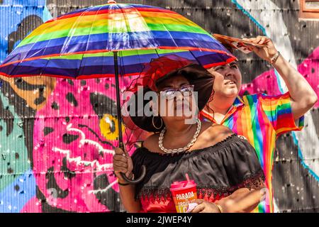 Goiânia, Goias, Brasilien – 05. September 2022: Zwei Menschen mit Regenschirm und farbenfroher Kleidung schauen nach oben. Foto während der LGBT-Parade in Goiania. Stockfoto