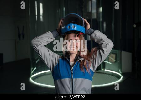 Kaukasische Frau setzt sich einen Helm an, bevor sie in einem Windkanal fliegt. Free Fall Simulator. Stockfoto