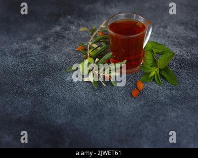 Tasse frisch gebrühten schwarzen Tee mit Minze und Mandelnüssen, warmes, weiches Licht, dunkler Hintergrund. Stockfoto