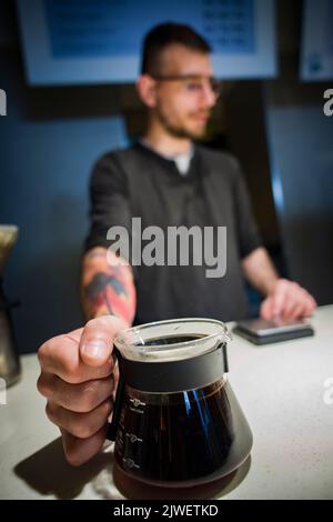 Ein Barista, der Kaffee in einem Glasgefäß serviert Stockfoto