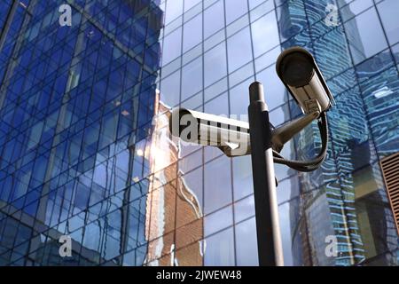 Überwachungsvideokameras im Freien auf dem Hintergrund des Wolkenkratzers. CCTV-Kamera in der Nähe des Business Centers, Konzept für Sicherheit, Privatsphäre und Schutz Stockfoto