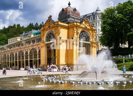 Marienbad, Tschechische Republik, 30. Juni 2022: Der singende Brunnen hinter den Kolonnaden des Kurortes mit einigen Touristen Stockfoto