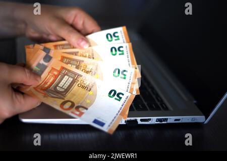 Euro-Banknoten in weiblichen Händen auf Laptop-Hintergrund. Frau, die Geld zählt, Konzept von Löhnen oder Bonus Stockfoto