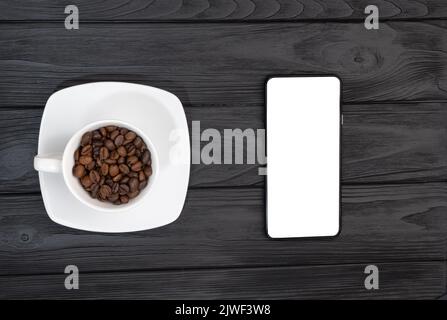 Draufsicht auf ein leeres Smartphone und eine Tasse Kaffee mit Bohnen. Weißer Leerraum für Werbelogo Stockfoto