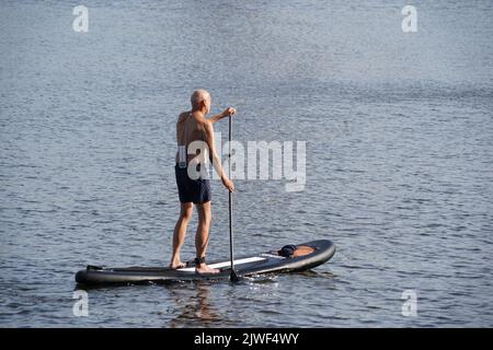 Der Mann, der auf einem Stand Up Paddle Board steht, paddelt auf einem See. Stockfoto