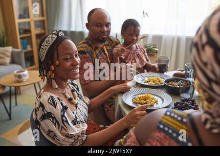 Afrikanisches glückliches Mädchen, das während des Feiertags-Abendessens am Tisch zu Hause mit ihrer Familie spricht Stockfoto