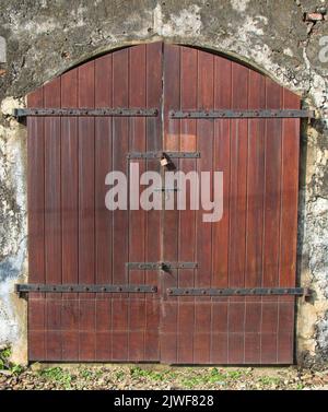 Alte Tür; alter Eingang eine Wand; alte Tür in einem Gebäude; Holztür auf einer braunen Waffenkammer; grauer Textureingang zu einem alten Kolonialhaus; Türmetall Stockfoto