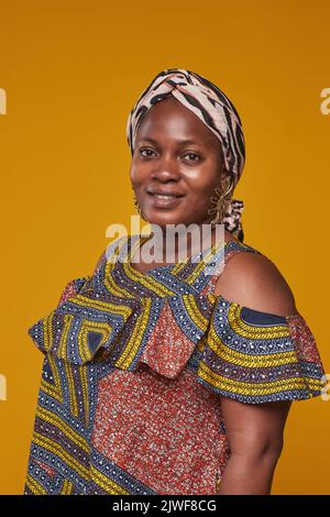 Porträt einer Afrikanerin in Nationaltracht, die lächelnd vor der Kamera vor gelbem Hintergrund steht Stockfoto
