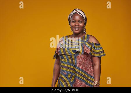 Porträt einer afrikanischen Frau in Nationalkostüm, die auf einem gelben Hintergrund vor der Kamera lächelt Stockfoto