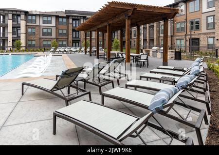 Blick auf die Chaiselongue-Stühle, den Swimmingpool und den Essbereich auf dem Dach in einem modernen Wohnkomplex im Hintergrund oder im Vorgarten Stockfoto