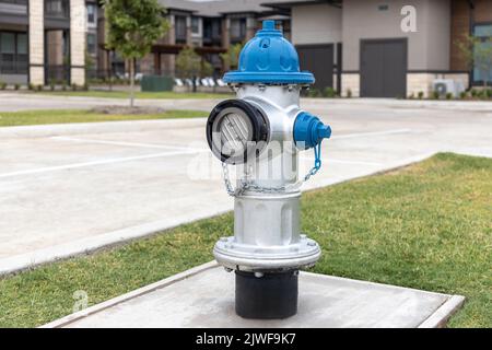 Grauer und blauer Hydrant auf Gehsteig im Hof in Wohnanlage mit Asphaltstraße und Gebäude im Hintergrund Stockfoto