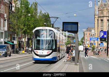 Amsterdam, Niederlande - August 2022: Moderne elektrische Straßenbahn, die an einer Straßenbahnhaltestelle im Stadtzentrum ankommt Stockfoto