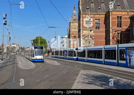 Amsterdam, Niederlande - August 2022: Moderne elektrische Straßenbahnen an einer Straßenbahnhaltestelle vor dem Hauptbahnhof der Stadt Stockfoto