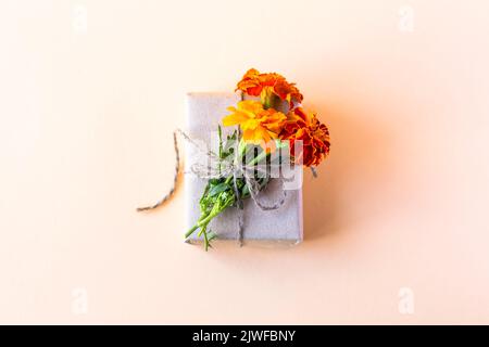 Geschenkbox in grauem Bastelpapier mit orangen Blumen verziert Ringelblumen auf orangefarbenem Hintergrund für den Urlaub, flach liegend Stockfoto