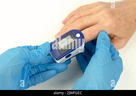 Messung der Sättigung bei einer 60-jährigen Frau. Arzthände in medizinischen Handschuhen Tragen Sie ein Pulsoximeter auf den Finger einer älteren Frau auf. Fürsorglich Stockfoto