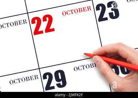 22. Tag im Oktober. Eine Hand, die einen roten Stift hält und auf das Kalenderdatum Oktober 22 zeigt. Rotes Kalenderdatum, Platz zum Kopieren, Modell. Herbst Monat, Tag o Stockfoto
