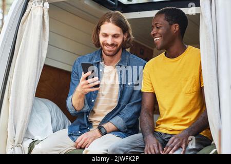 Freunde sehen lustige Videos auf dem Handy und lachen, während sie im Wohnmobil sitzen Stockfoto