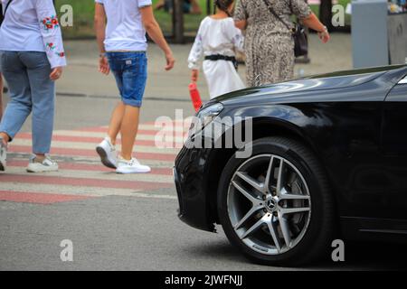 Auto Mercedes-Benz passiert Menschen auf einer Fußgängerüberfahrt Stockfoto