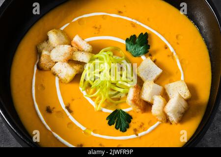 Karottenpüree-Suppe mit Croutons und Lauch auf dunklem Grund Stockfoto