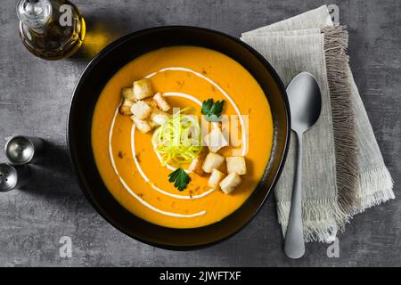 Karottenpüree-Suppe mit Croutons und Lauch auf dunklem Grund Stockfoto