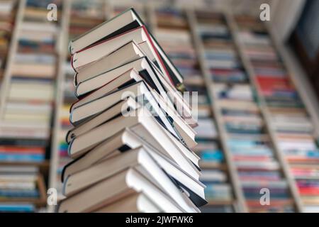 Turm mit gestapelten Romanen vor der Bücherwand Stockfoto