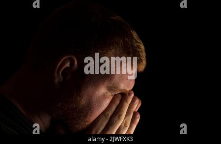 Erwachsener kaukasischer Mann, der den Kopf in den Händen hält und nach unten blickt. Stockfoto