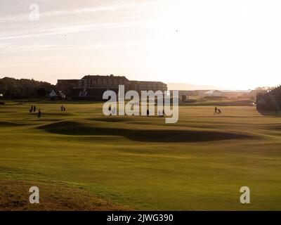 Die Golfer, die während des Sonnenuntergangs über den wunderschönen und legendären Old Course in St. Andrews in Schottland wandern Stockfoto