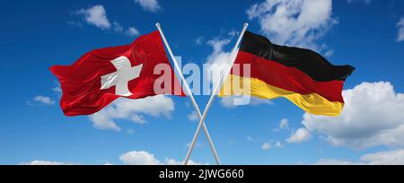 Zwei gekreuzte Flaggen Bundesrepublik Deutschland und Schweiz winken im Wind bei bewölktem Himmel. Konzept von Beziehung, Dialog, Reisen zwischen zwei Co Stockfoto